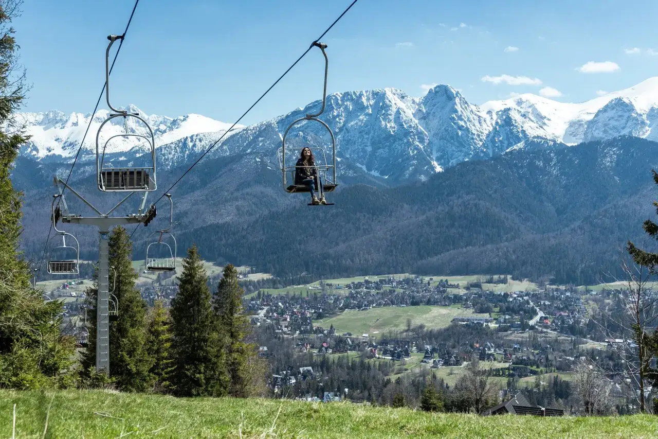 Wyciąg krzesełkowy na Gubałówkę z widokiem na ośnieżone Tatry. Kobieta w kolejce na górę podziwia panoramę.