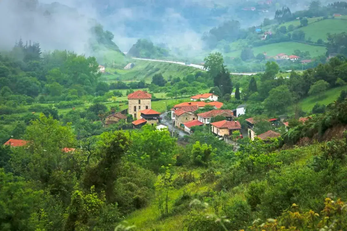 Mglisty poranek nad wioską, przez którą biegną jedne z tras Camino de Santiago. Zielone wzgórza i tradycyjna zabudowa tworzą malowniczy krajobraz.