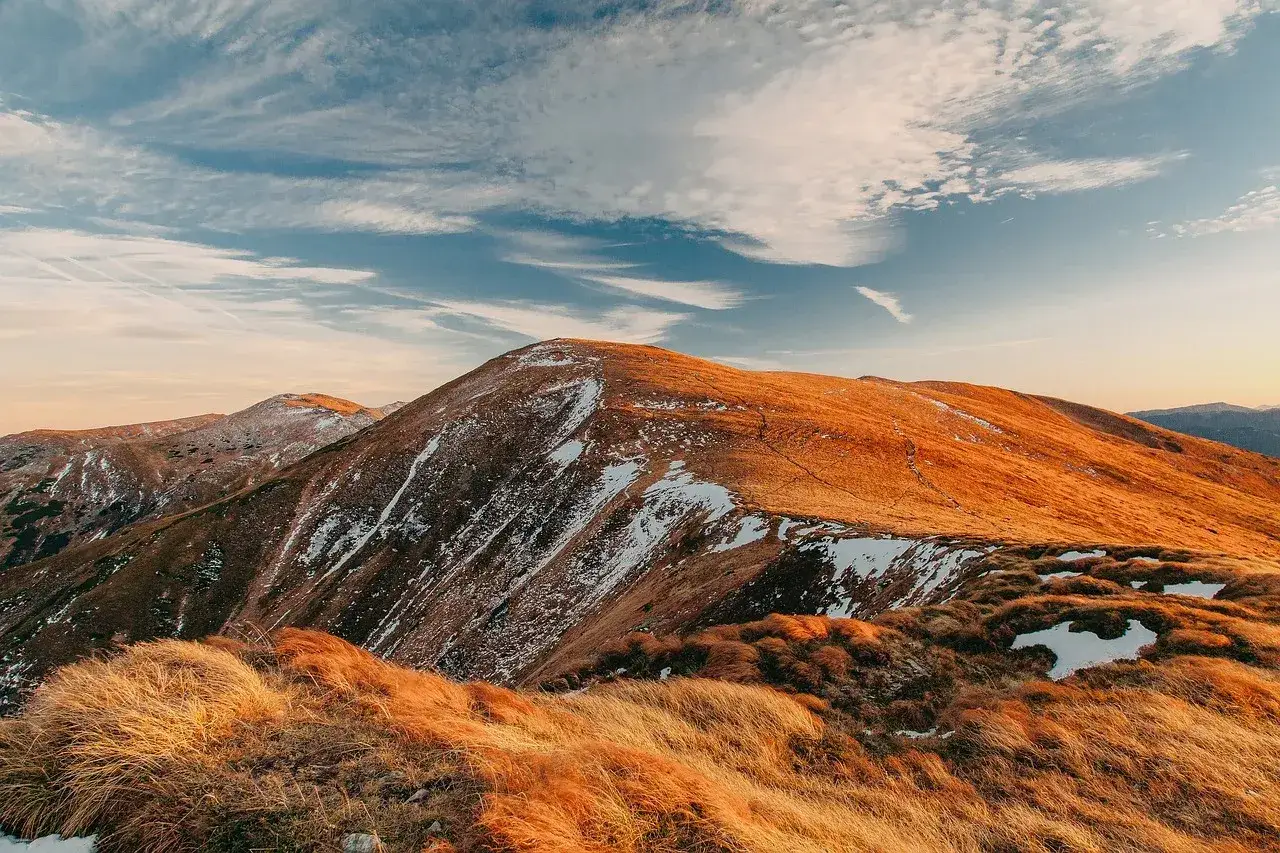 Złote trawy i śnieg na zboczach gór tworzą malowniczy krajobraz. Szlak papieski Tatry w jesiennym słońcu.