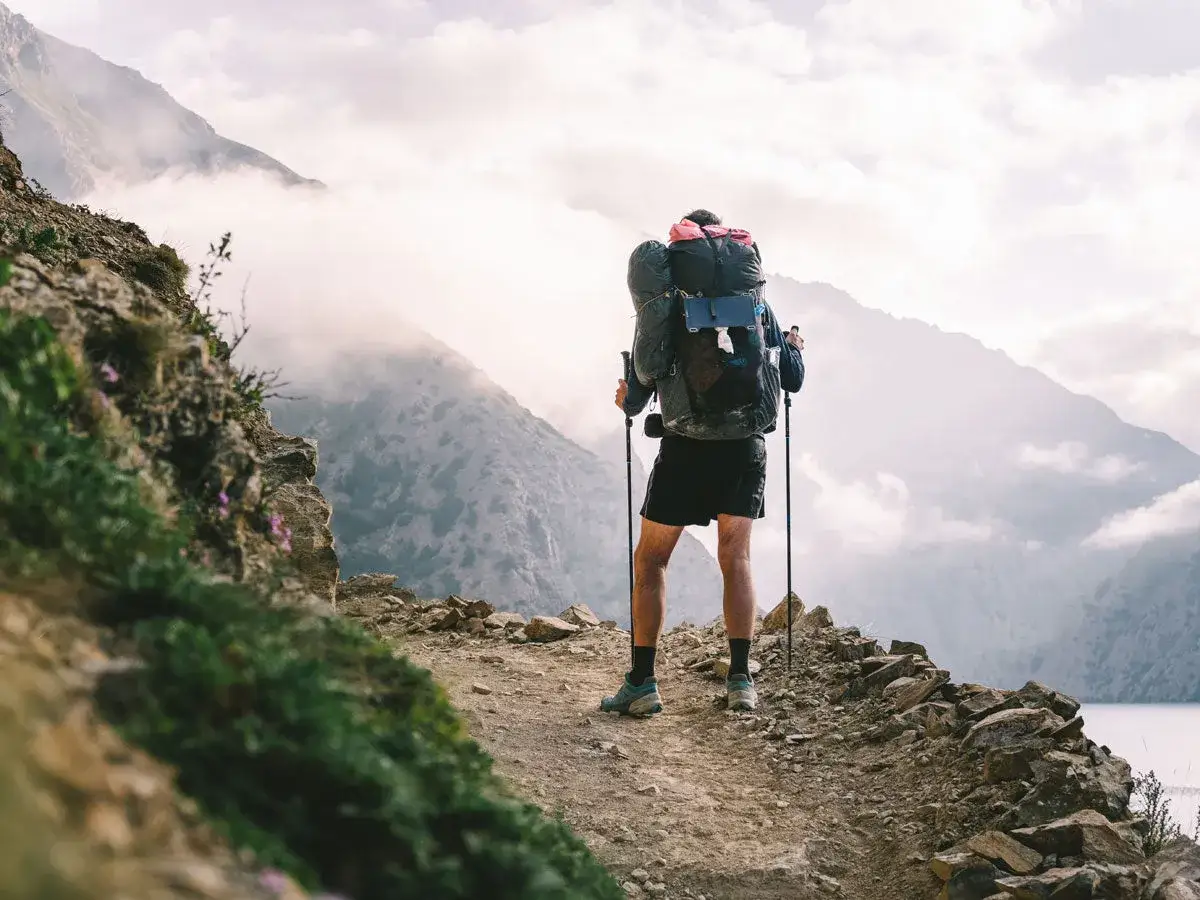 Trekking w Himalajach. Samotny turysta z plecakiem i kijkami przemierza skalistą ścieżkę na tle mglistych gór.