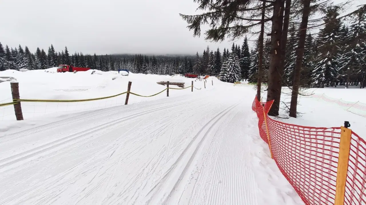 Trasa na narty biegowe Jakuszyce przygotowana, w tle czerwony ratrak. Śnieg i las tworzą zimowy krajobraz.