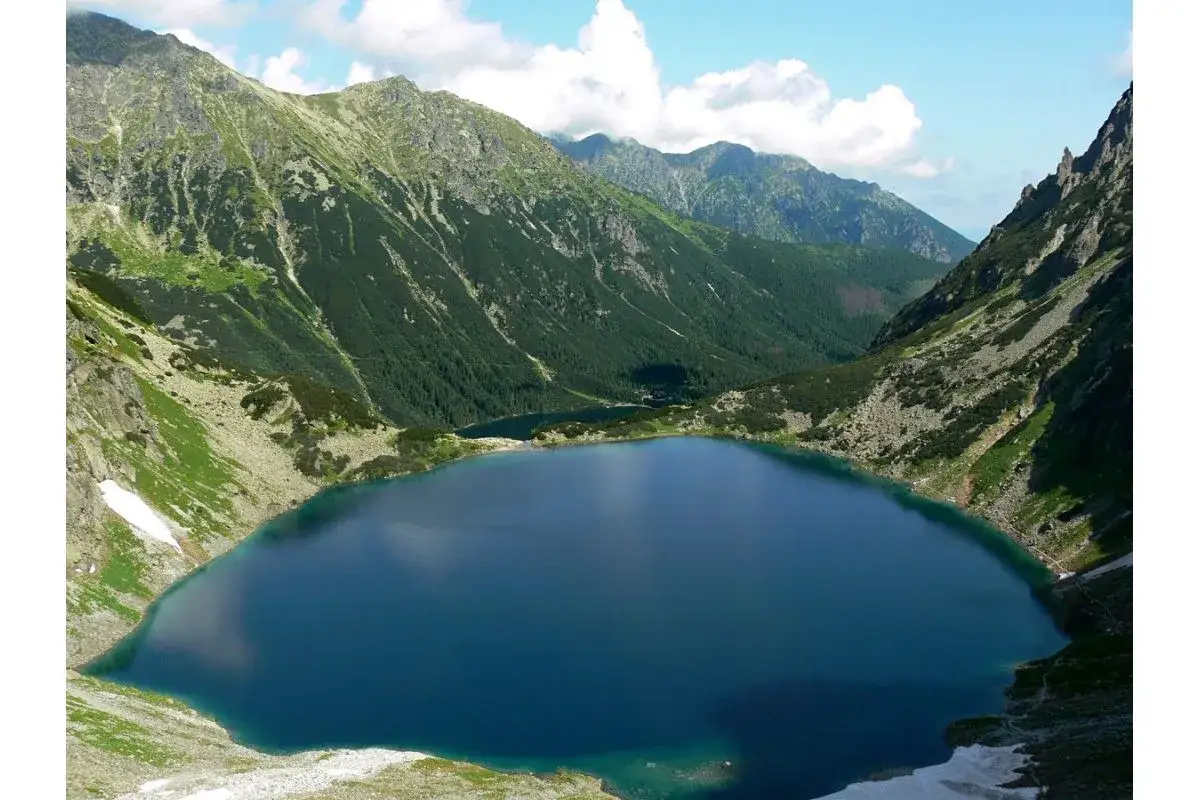 Głęboki, granatowy staw pod Rysami, otoczony stromymi, zielonymi zboczami g&oacute;r. W oddali widać kolejne jezioro.
