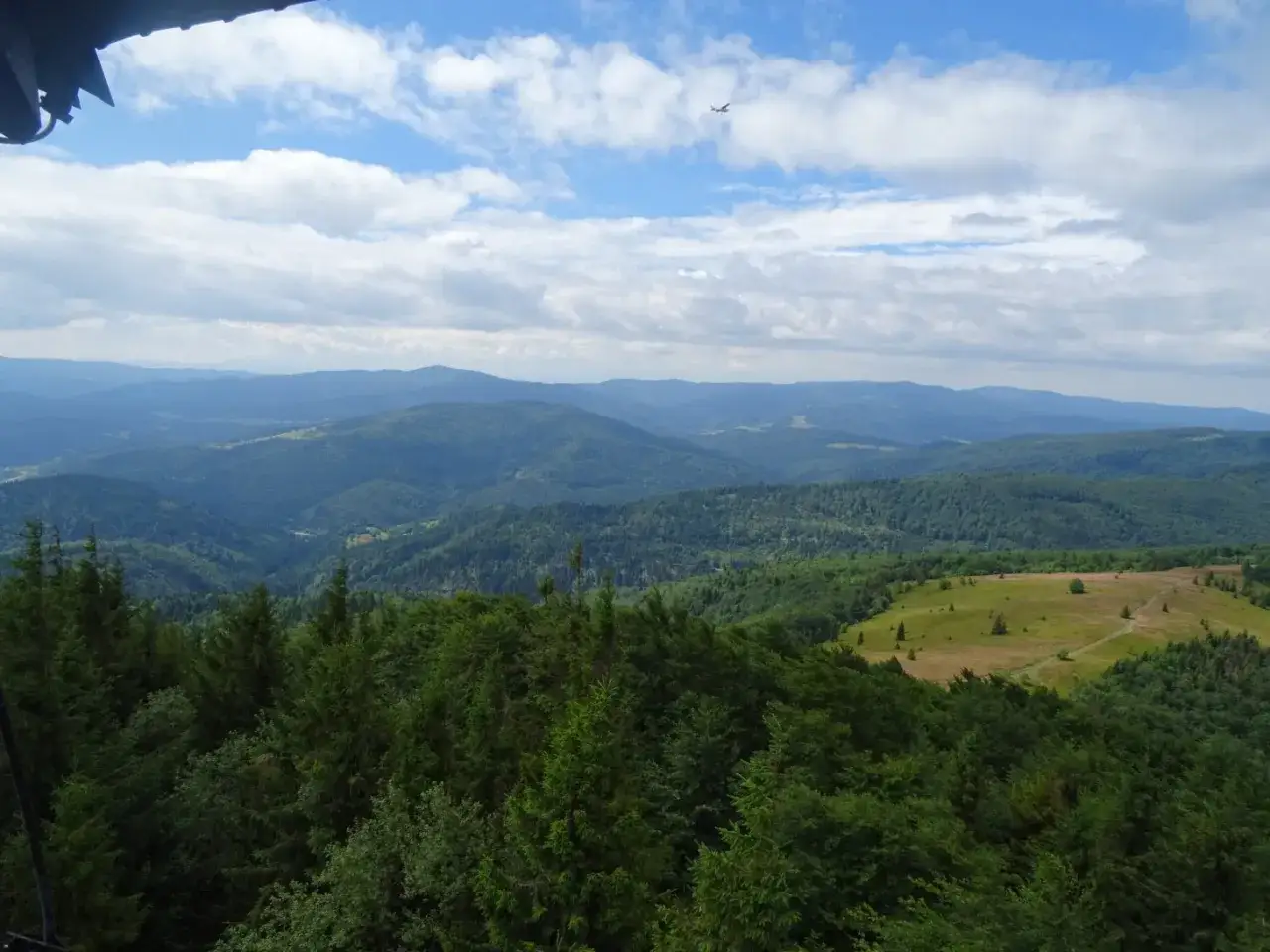 Widok z Mogielicy z Jurkowa na Beskid Wyspowy. W oddali widać pasmo górskie, a na niebie leci samolot.