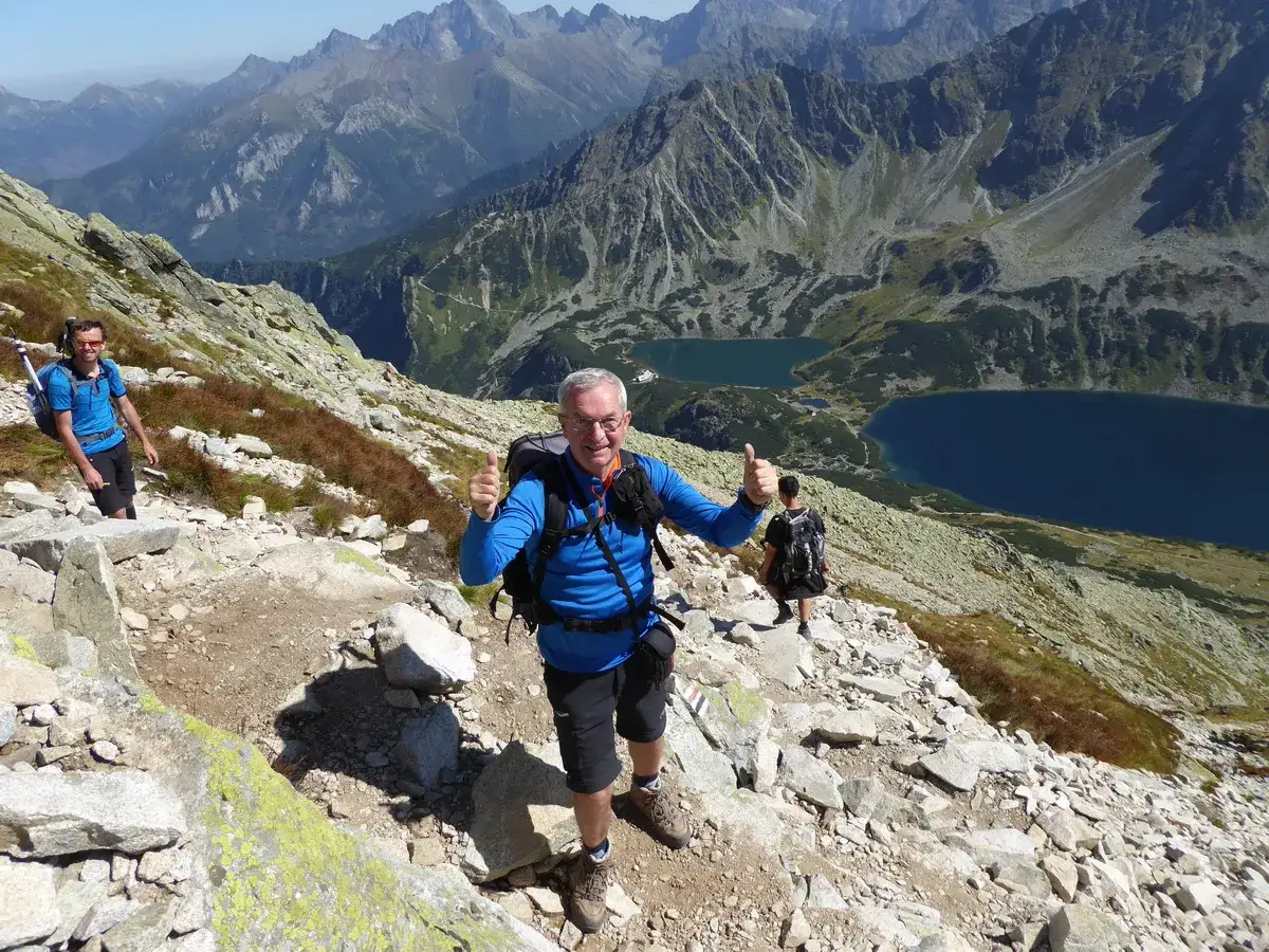 Szlak na Kozi Wierch z Doliny Gąsienicowej. Trzech turystów wędruje kamienistym szlakiem, podziwiając widok na Tatry i Morskie Oko.