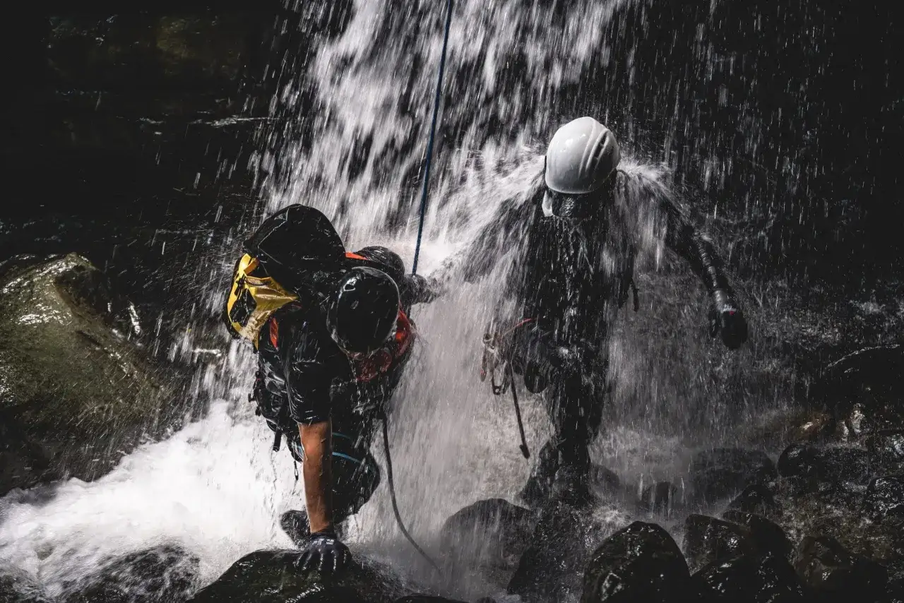 Dwóch ludzi w kaskach i sprzęcie zjazdowych pokonuje wodospad. To właśnie jest canyoning – ekstremalna przygoda w kanionach.