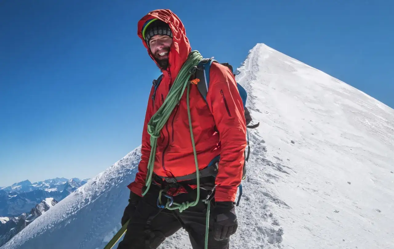 Uśmiechnięty alpinista w czerwonej kurtce na szczycie, gotowy na wejście na Mont Blanc.