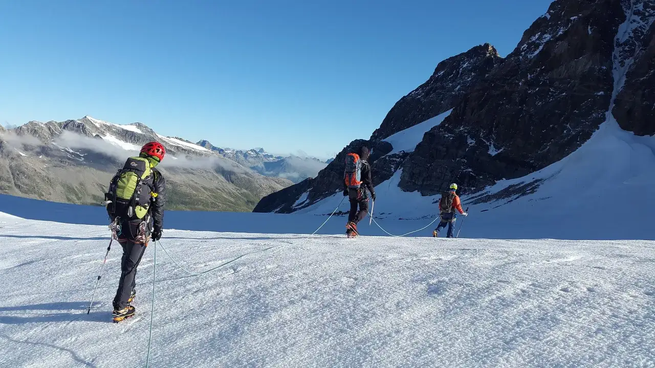 Trzej alpiniści na lodowcu, uczący się, jak zostać przewodnikiem górskim. W tle majestatyczne szczyty.