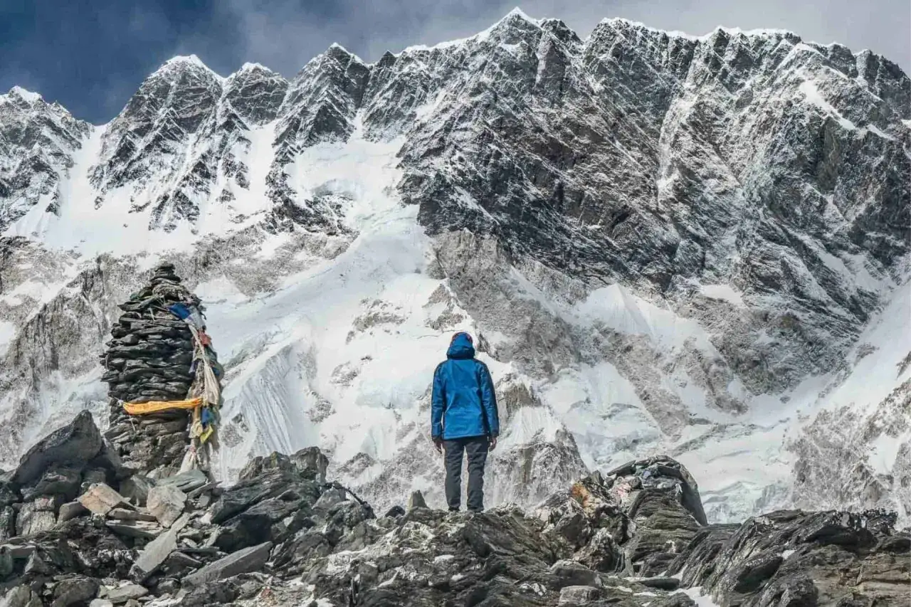 Osoba w niebieskiej kurtce podziwia majestatyczne szczyty podczas trekkingu w Himalajach. Kamienny kopiec z flagami modlitewnymi dodaje mistycznego charakteru.