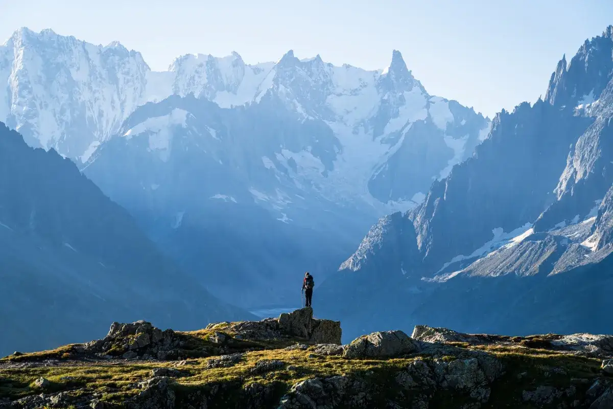 Turysta na szczycie skalistego wzgórza, podziwiający majestatyczne Alpy podczas trekkingu Tour du Mont Blanc.