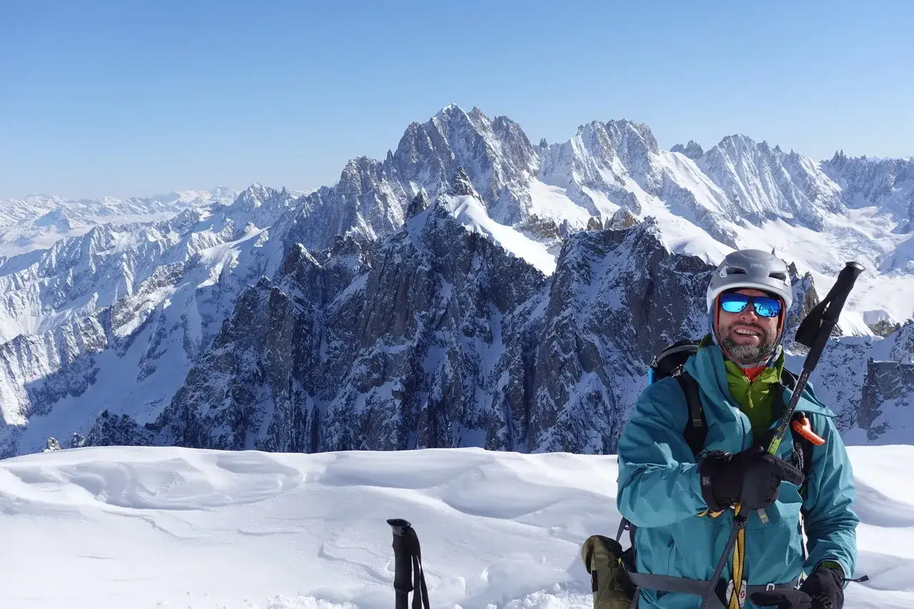 Uśmiechnięty narciarz w kasku i goglach na tle majestatycznych, ośnieżonych szczytów. To niezapomniane Mont Blanc latem, gdzie śnieg wciąż króluje.
