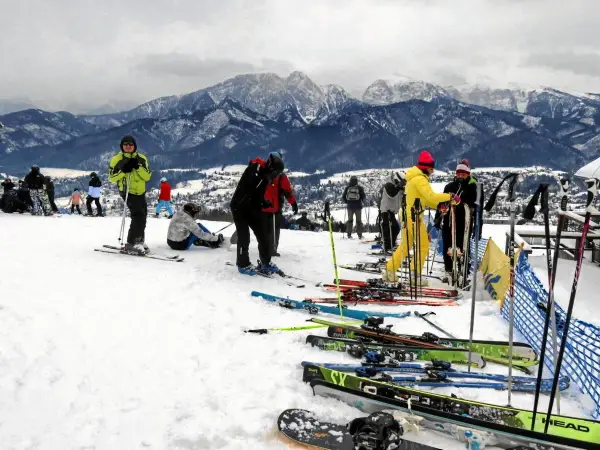 Ludzie na nartach i snowboardach na stoku, w tle góry. Zastanawiasz się, ile się idzie na Gubałówkę? Tu jest zimowo i aktywnie!