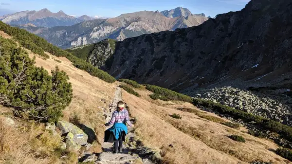 Osoba wędruje kamienistym szlakiem w Tatrach. Widok na góry i dolinę, idealne tatry szlaki dla średnio zaawansowanych.