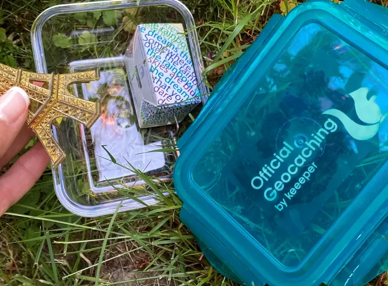 Złoty model Wieży Eiffla w pojemniku, obok niebieskiego pojemnika z napisem "Official Geocaching". To jest geocaching co to za zabawa!